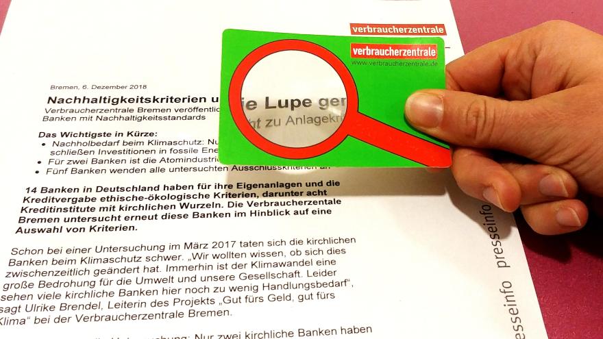 Hand mit Lupe auf Pressemitteilung Verbraucherzentrale Bremen